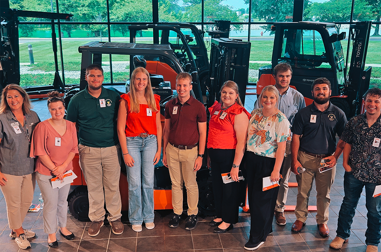 College-aged students smiling and standing in front of farm equipment.