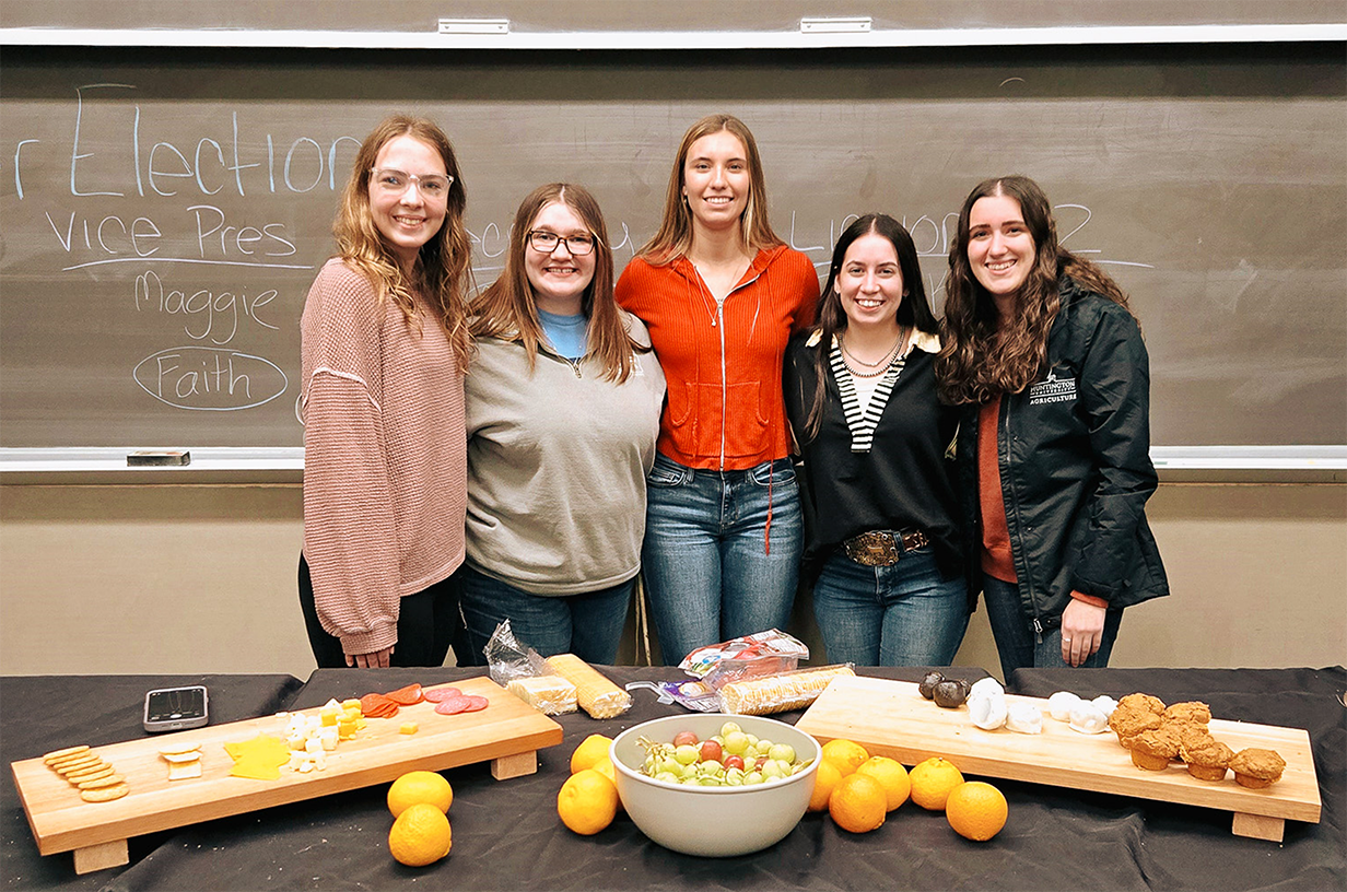 A group of college-aged women smiling in front of a charcuterie board.