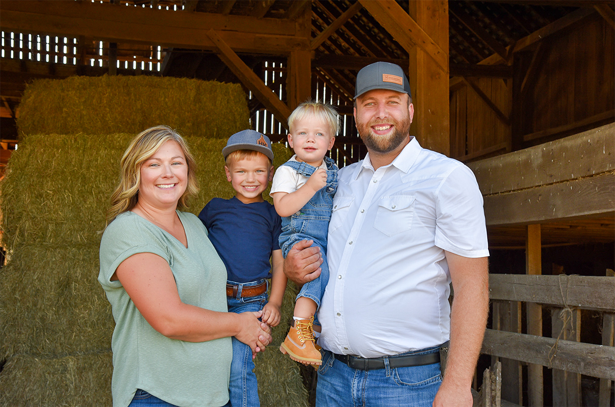 A family smiling with hay and a barn behind them.