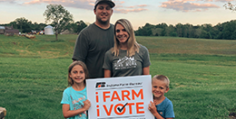 Family standing in front of a sign that says "I Farm, I Vote".