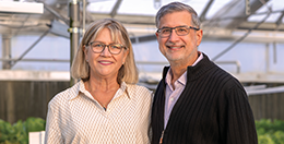 A smiling couple stands in a greenhouse.